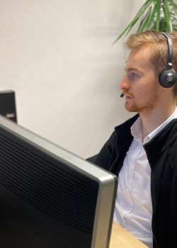 Ein Mitarbeiter sitzt mit einem Headset an einem Schreibtisch und schaut auf den Monitor.